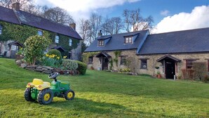 A green tractor on a lawn in front of a stone building with a sloped roof and a small window.