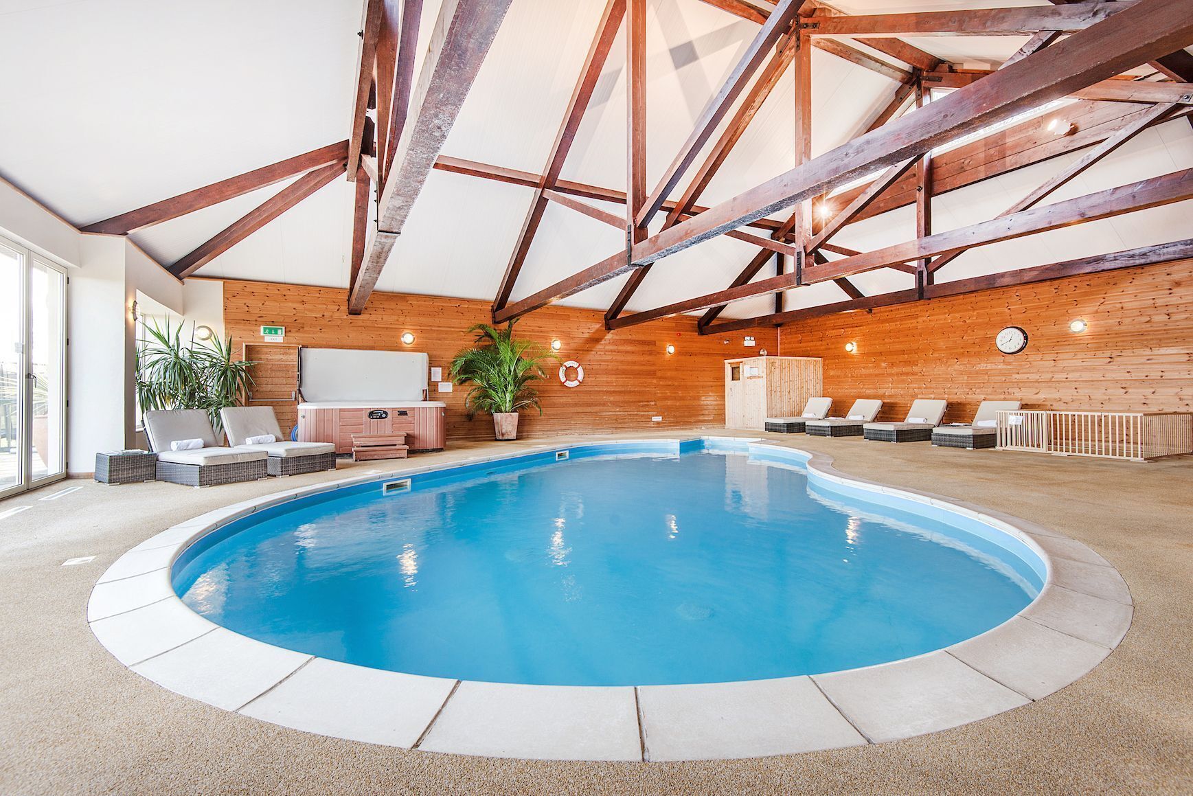 Ein Innenpool mit Holzbalkendecke und -wänden, umgeben von Liegestühlen und einem Whirlpool.