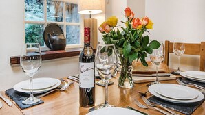 A dining table set with plates, cutlery, wine glasses, and a bottle of wine. There is a vase with flowers and a lamp on the table.