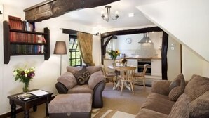 A cozy living room with a sofa, ottoman, and a coffee table, a bookshelf, and a dining area with a table and chairs. - A delightful two bedroom cottage with exceptional indoor leisure facilities (Boncath)