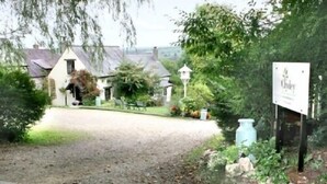 A rural property with a gravel driveway leading to a white building with a gabled roof. There are trees and shrubs around, and a birdhouse is visible. - A delightful two bedroom cottage with exceptional indoor leisure facilities (Boncath)