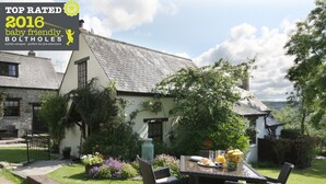 A traditional house with a stone exterior, a tiled roof, and a well-maintained garden with a dining table set for breakfast. - A delightful two bedroom cottage with exceptional indoor leisure facilities (Boncath)