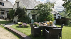 A traditional house with a stone exterior, a tiled roof, and a well-maintained garden with a dining table set for breakfast.