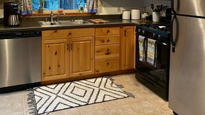 Una cocina con gabinetes de madera, electrodomésticos de acero inoxidable, un ventanal con cortinas y una alfombra estampada.