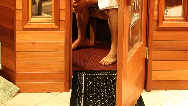 A wooden sauna room with a glass door, a bench, and a towel rack.
