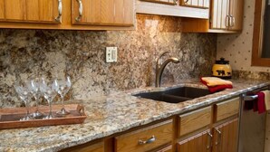 A kitchen with granite countertops, wooden cabinets, a stainless steel sink, and a red towel hanging on the door.