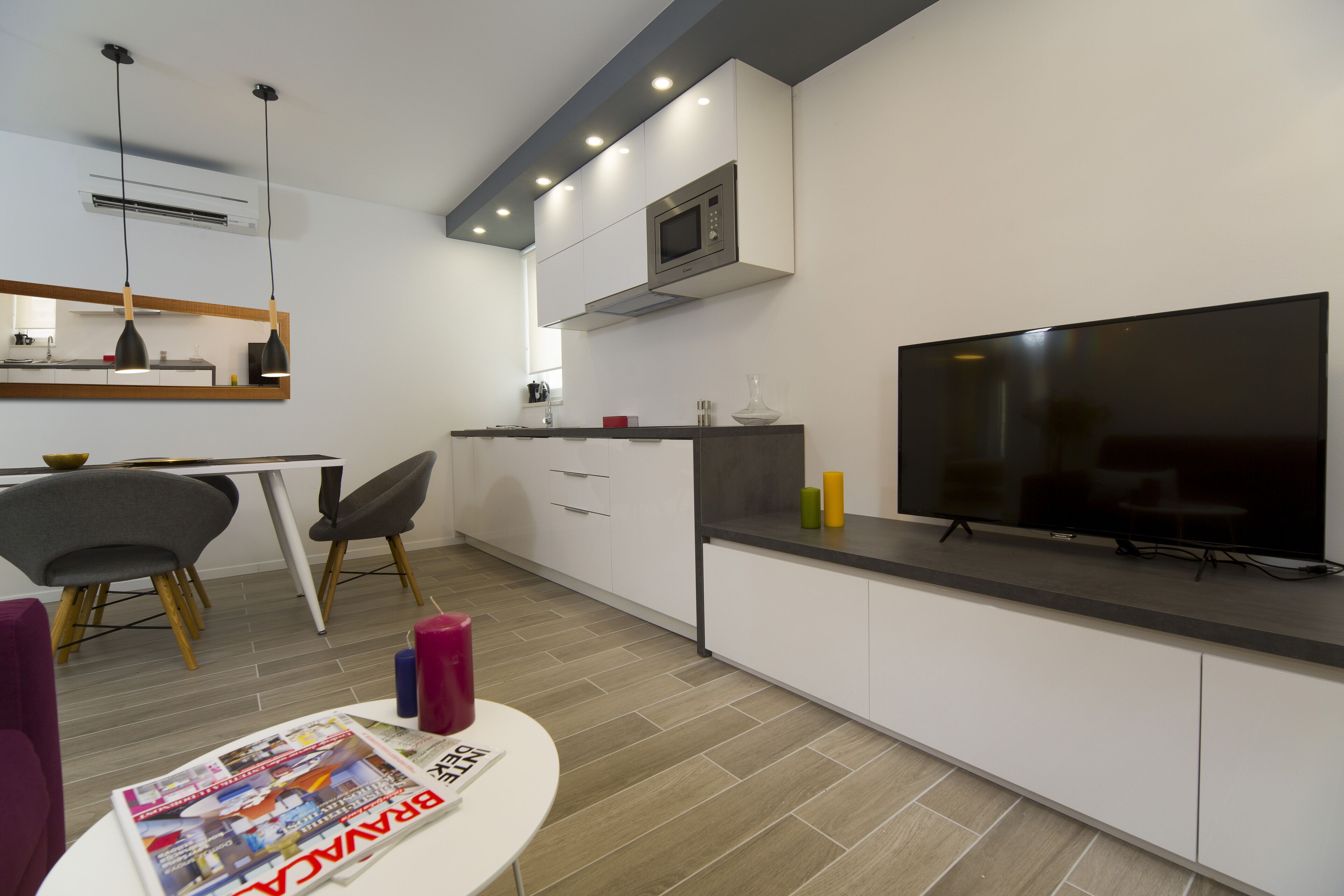 A modern kitchen with a built-in microwave, a dining area with chairs, and a flat-screen TV on the counter.