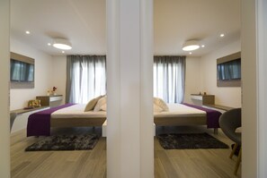 Reflejo de un dormitorio moderno con cama, mesitas de noche, escritorio y silla.