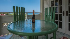 A glass table with a bottle and two wine glasses on a balcony with green chairs and a view of the ocean. - Mystic Ridge Resort (Ocho Rios)
