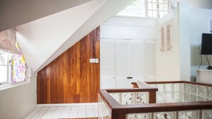 A room with wooden flooring, white walls, a wooden sloped ceiling, a white door with shutters, and a glass railing. - Mystic Ridge Resort (Ocho Rios)