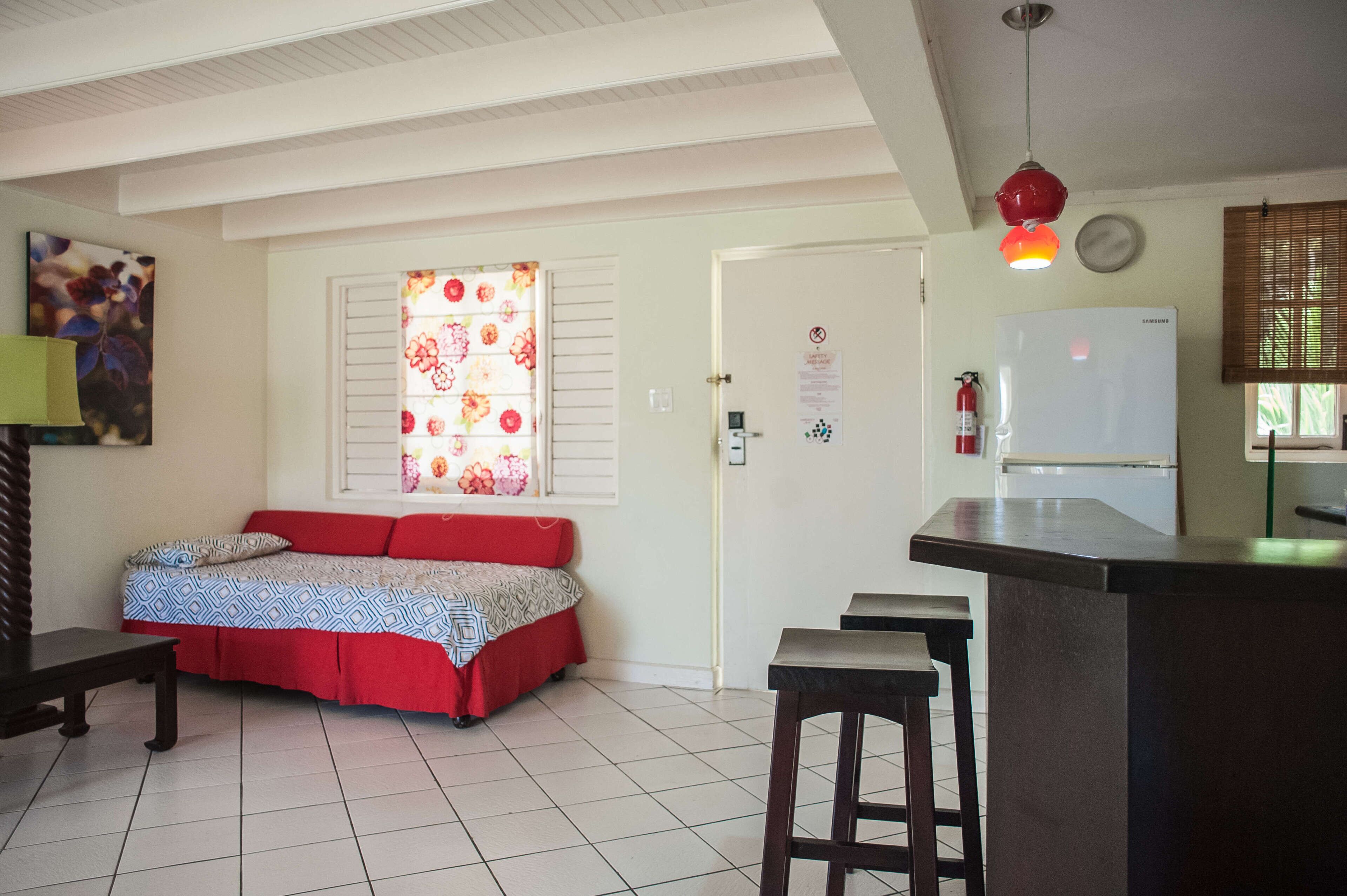 Une chambre comprenant un lit, une petite table, un coin bar, un réfrigérateur et une fenêtre avec des stores.
