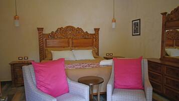 A bedroom with a wooden bed, two chairs with pink cushions, a small round table, and a dresser with a mirror.