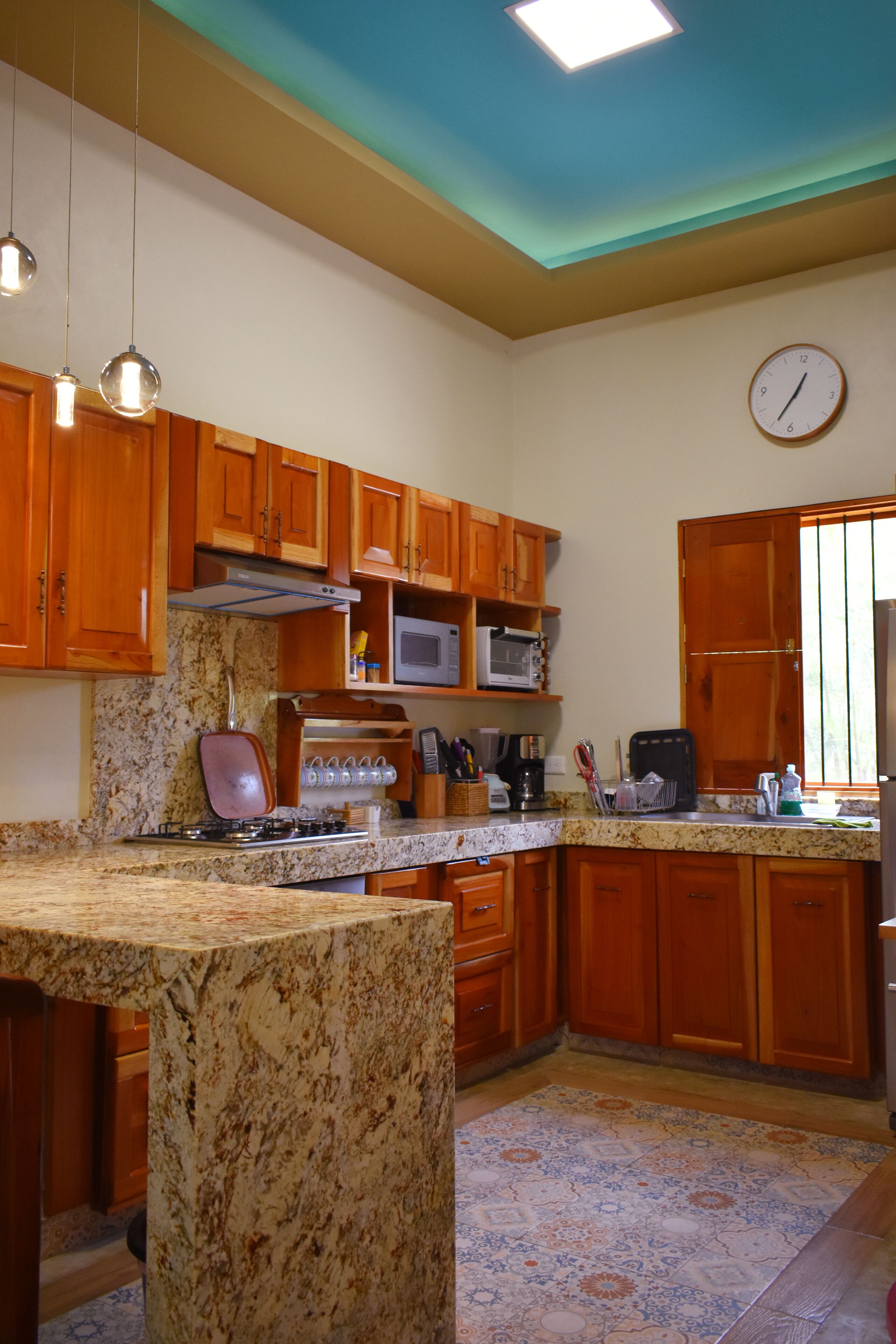 Una cocina con armarios de madera, un microondas, una estufa y un reloj en la pared.