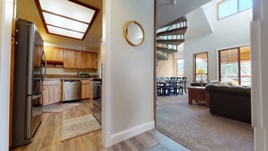A spacious kitchen with wooden cabinets, a refrigerator, and a microwave. There is a dining area with a table and chairs, and a living room with a sofa. A staircase leads to an upper level. - Aspen 230-Walking distance to the ski area with views of Mammoth Mountain! (Mammoth Lakes)