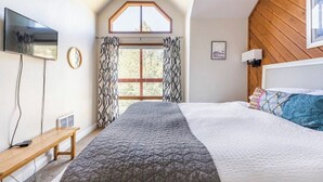 A bedroom with a large bed, a TV mounted on the wall, a window with curtains, and a wooden ceiling. - Aspen 230-Walking distance to the ski area with views of Mammoth Mountain! (Mammoth Lakes)