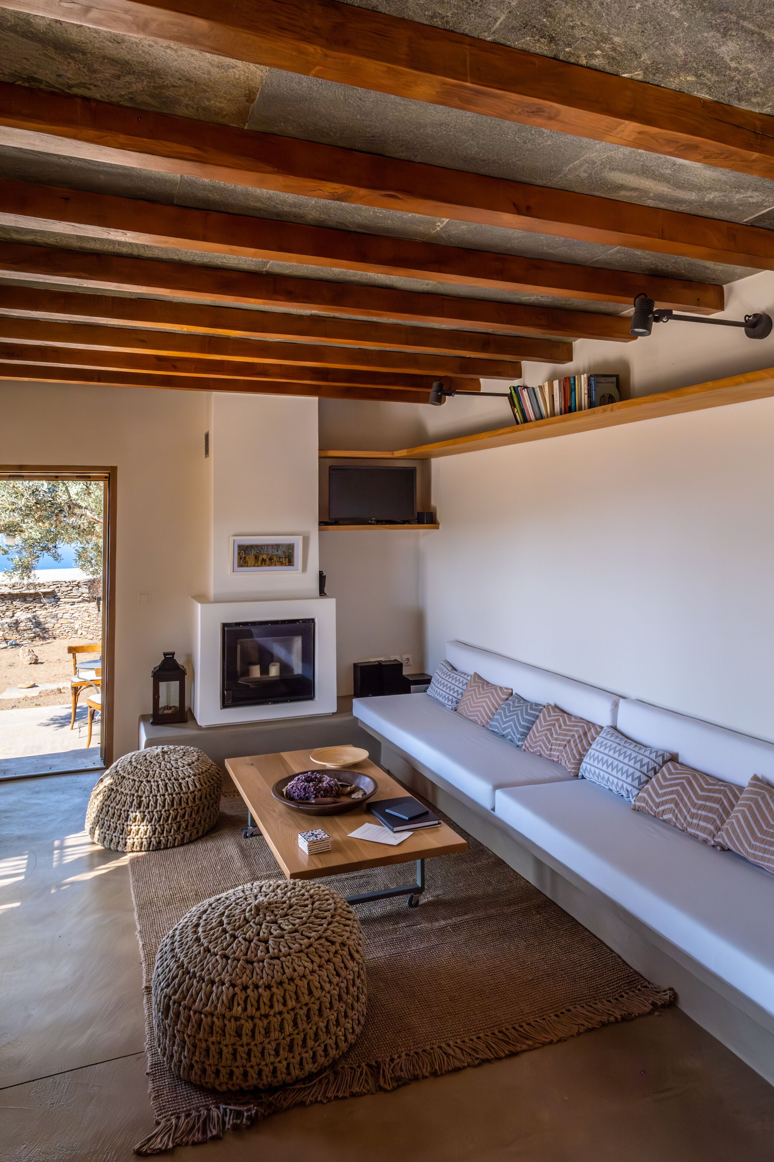 A modern living room with a fireplace, white sofa, and wooden beams on the ceiling.