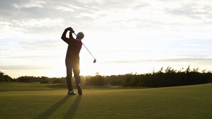 Silhouet van een persoon die golf speelt op een golfbaan met een heldere lucht.