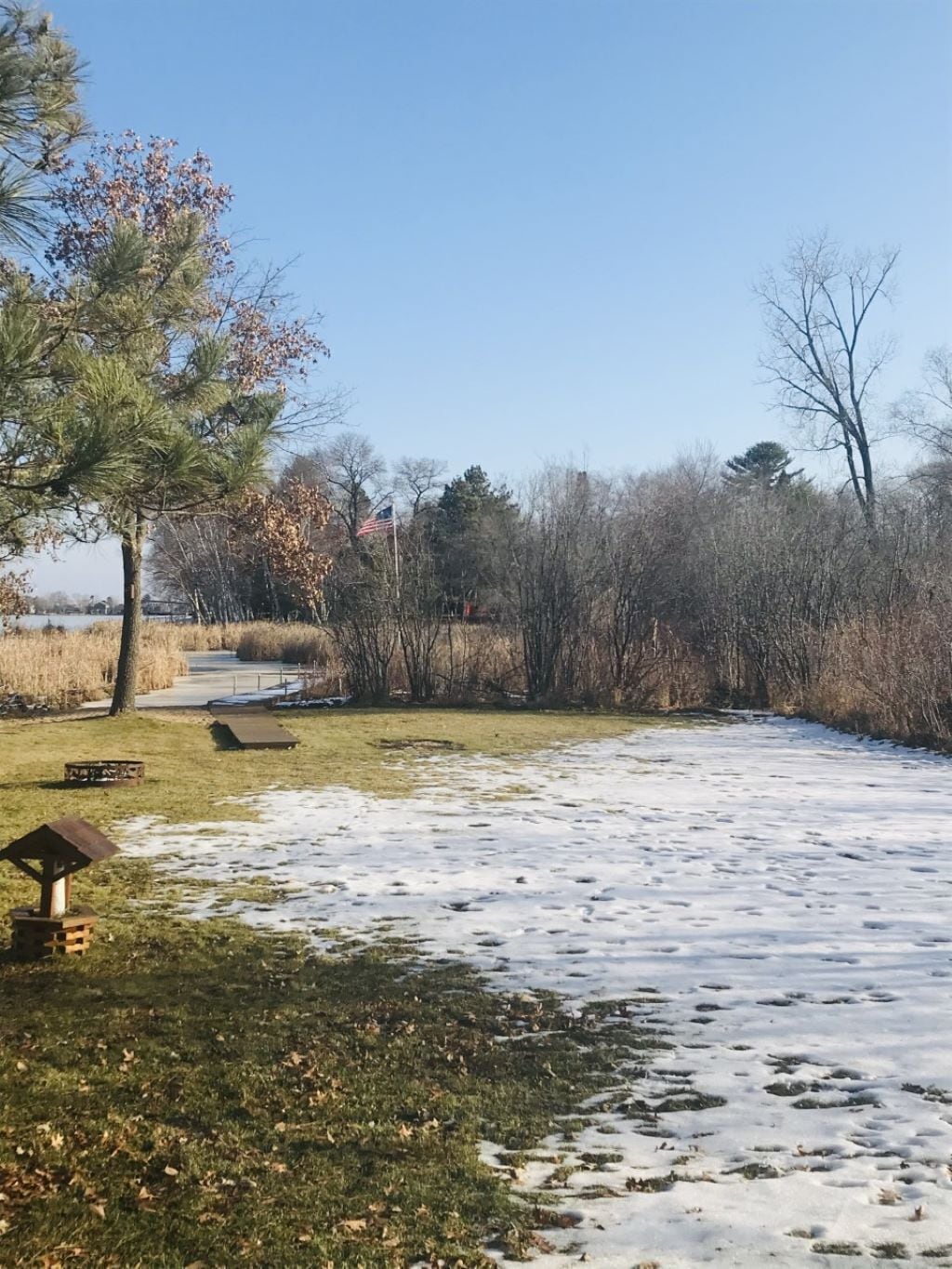 Un parc dont le sol est recouvert de neige, avec une table de pique-nique et un mât pour drapeau.