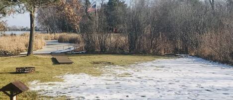Un parc dont le sol est recouvert de neige, avec une table de pique-nique et un mât pour drapeau.