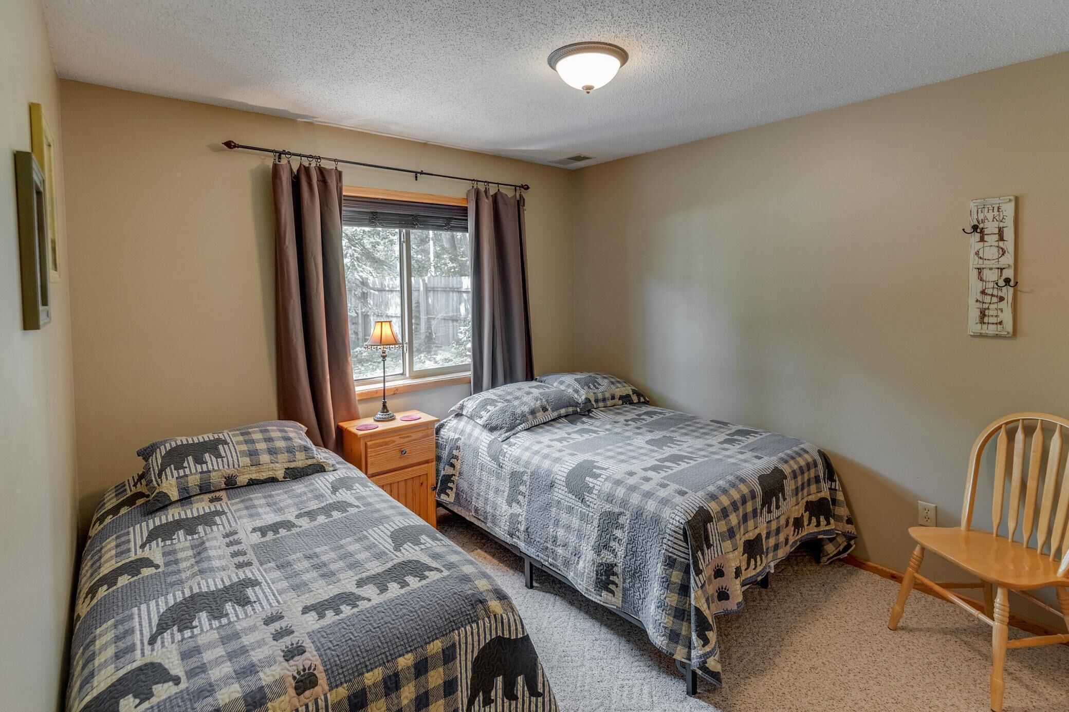 A bedroom with two beds, a nightstand, a chair, a window with curtains, and a wall decoration.