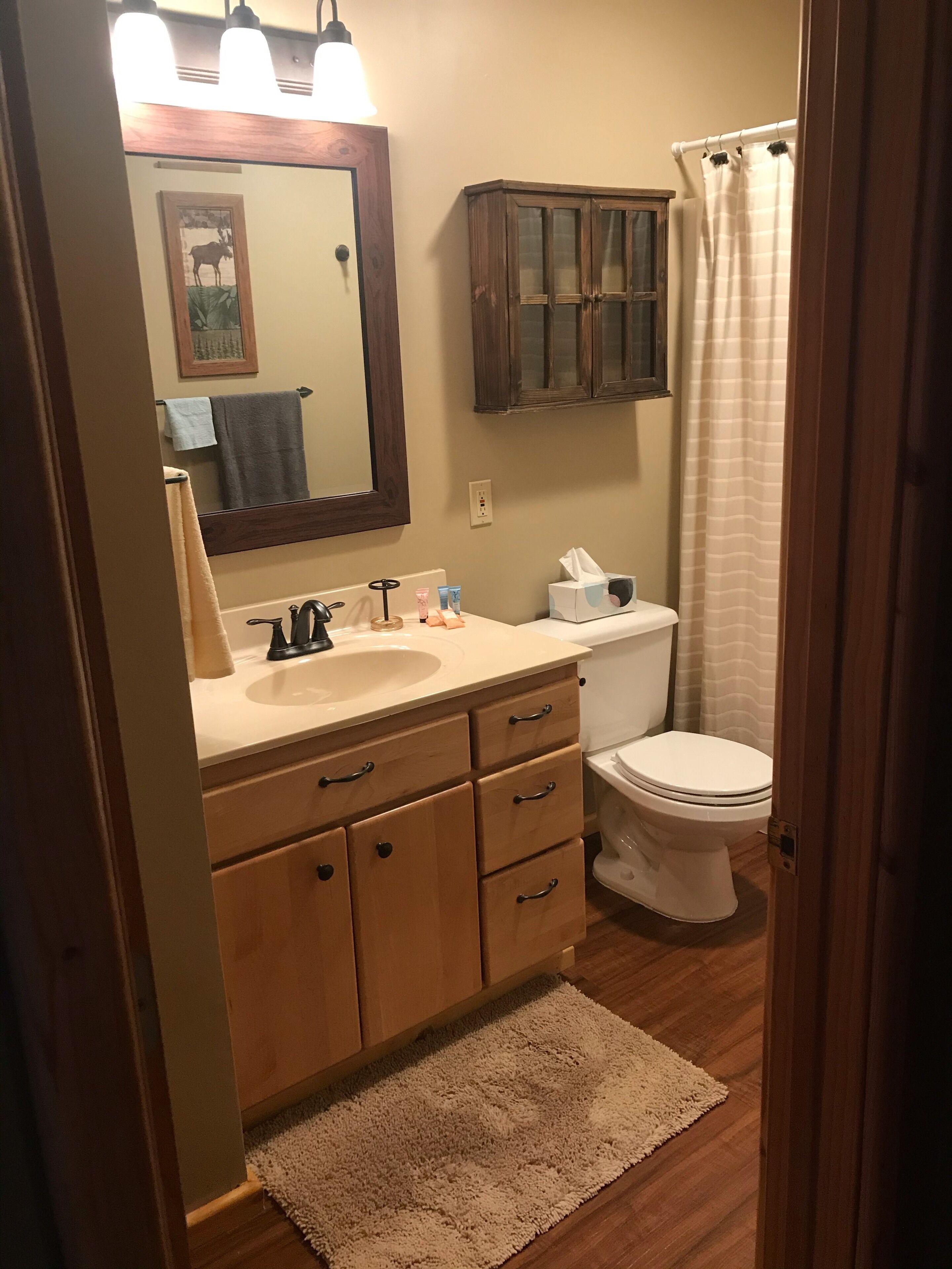 A bathroom with a wooden vanity, a sink, a mirror, a toilet, and a shower curtain.