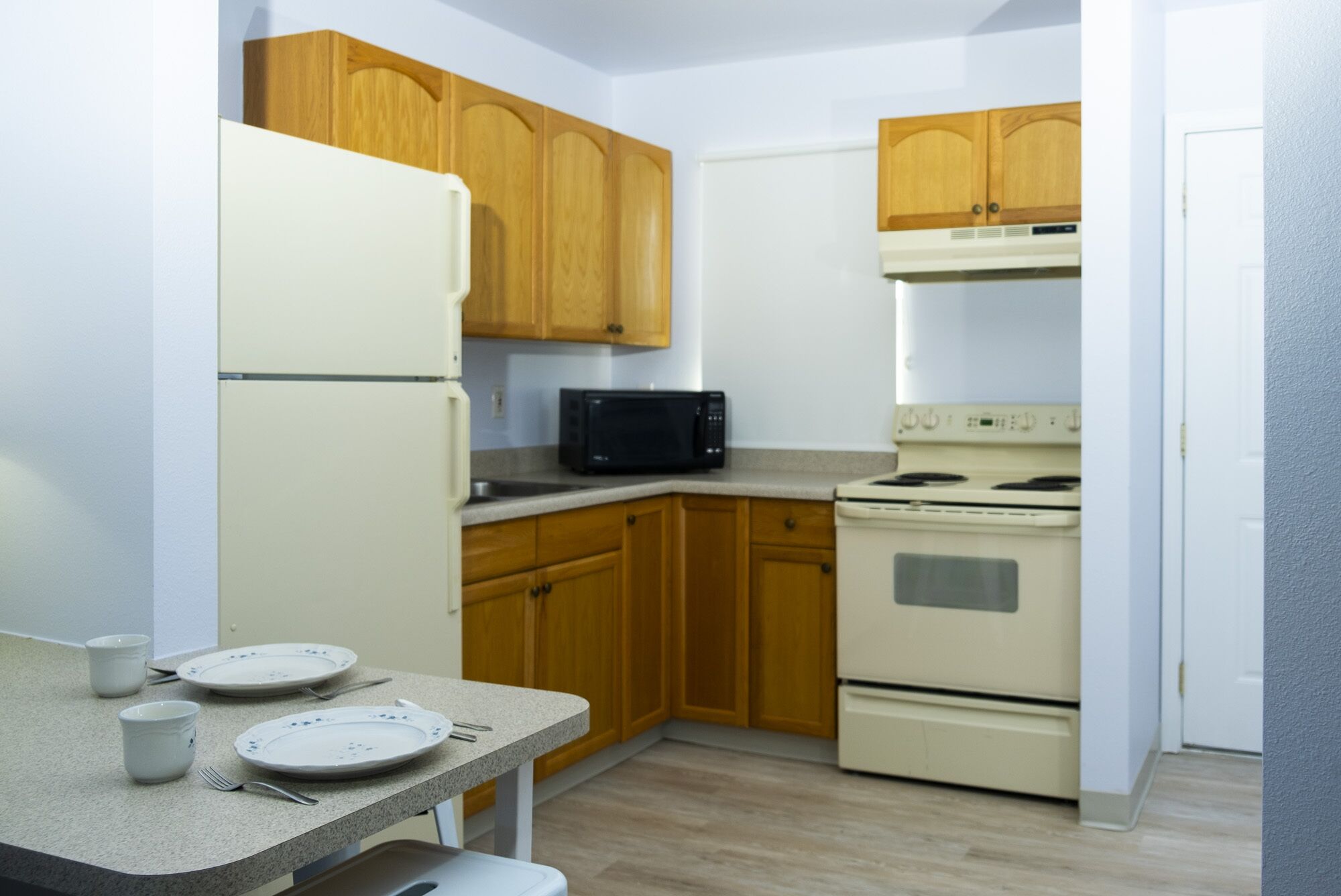 A compact kitchen with wooden cabinets, a white refrigerator, a microwave, and a stove.