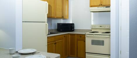 A compact kitchen with wooden cabinets, a white refrigerator, a microwave, and a stove.