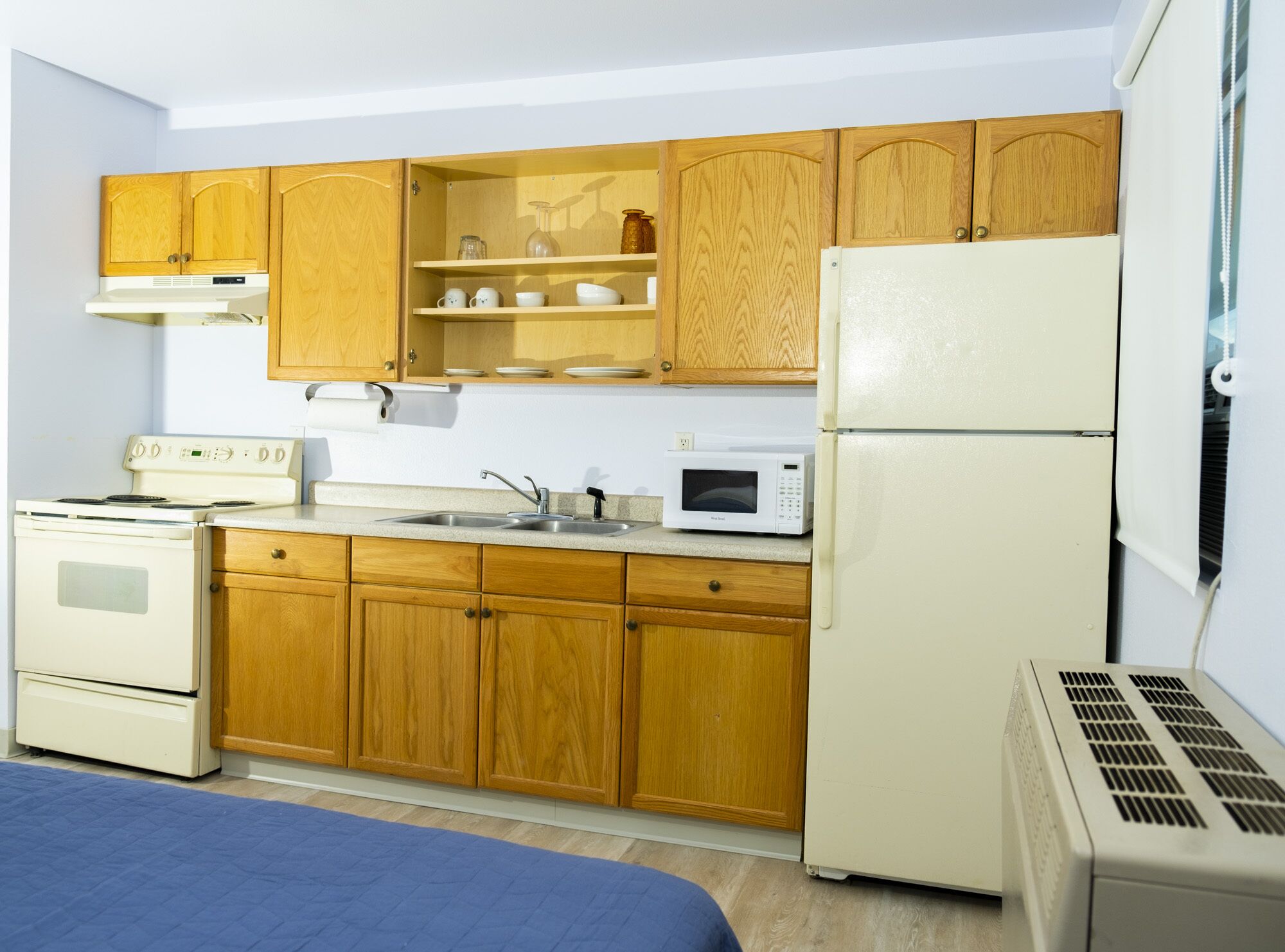 A compact kitchen with wooden cabinets, a white stove, a microwave, and a refrigerator.