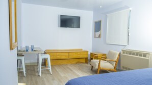 Ein Schlafzimmer mit Bett, Schreibtisch, Stuhl, Kommode, Heizkörper und Fernseher.