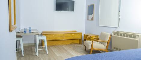 Un dormitorio con cama, escritorio, silla, cómoda, radiador y televisor.