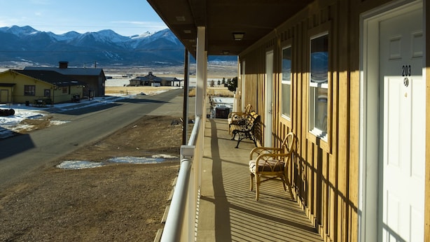 Ein Motel mit einer überdachten Veranda, Blick auf Berge und einer Straße mit Gebäuden im Hintergrund.