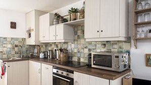 A modern kitchen with white cabinets, a wooden countertop, a microwave, and a tiled backsplash. - 3 Victoria House, St Ives – Sleeps 4 – Sea Views (St Ives)