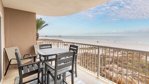 Ein Balkon mit Tisch und Stühlen, der Blick fällt auf einen Strand mit Zaun und Palmen.