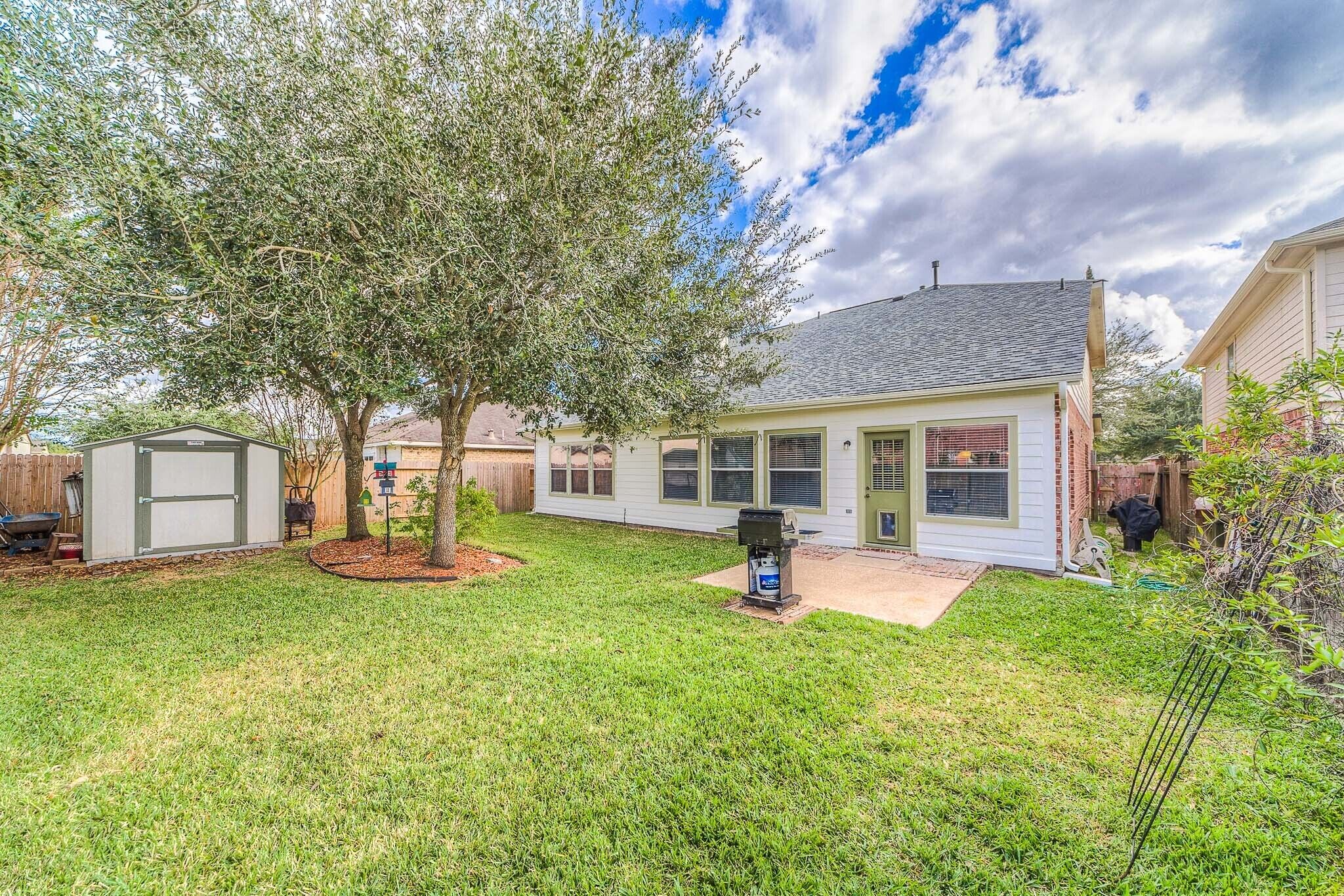 A residential backyard with a house, a tree, a shed, and a grill.
