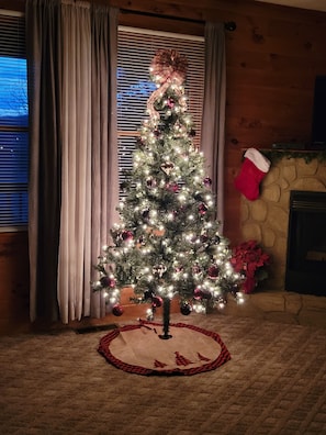 Um pinheiro de Natal com luzes e enfeites, lareira e um enfeite natalino.