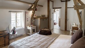 Ein Schlafzimmer mit einem großen Bett, Holzboden, einem Fenster und einem kleinen Tisch mit einem Korb.