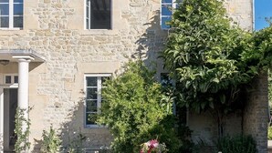 A stone building with a dining area set up outside. There are tables with chairs, a white tablecloth, and a variety of tableware. - Charming B&B close to the D-day beaches and to Bayeux (Mosles)