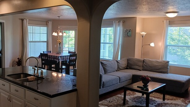 A kitchen with a stainless steel refrigerator, a sink, and a dining area with a table and chairs. There is a sofa and a coffee table in the living area. - Beautiful Condo in South Jordan Utah (South Jordan)