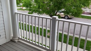 A porch with a white railing, a black chair, and a view of a street with a tree and a white picket fence. - Beautiful Condo in South Jordan Utah (South Jordan)