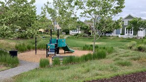A playground with a slide and climbing structures, surrounded by grass and trees, with houses in the background. - Beautiful Condo in South Jordan Utah (South Jordan)