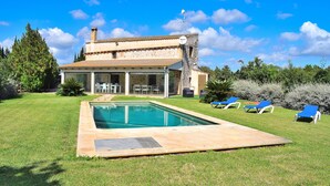 A house with a swimming pool, a patio with lounge chairs, and a garden.