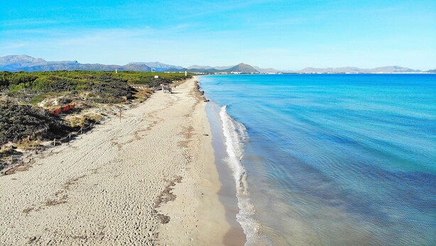 A beach with clear blue water, a sandy shore, and distant mountains.