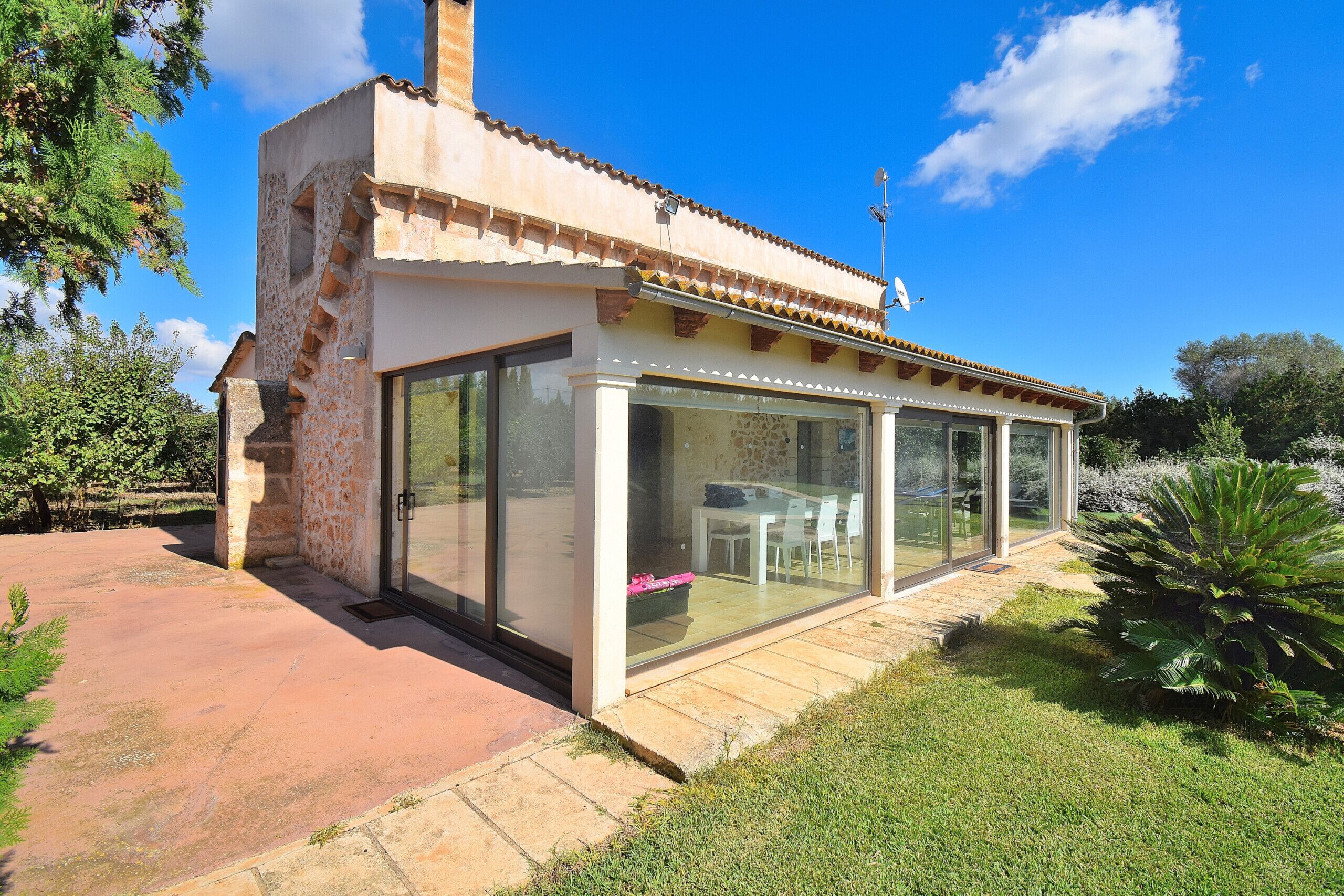 A modern house with a glass-enclosed patio, stone walls, and a clear blue sky.