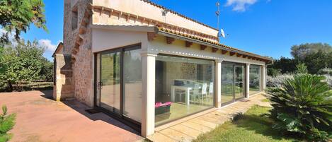 A modern house with a glass-enclosed patio, stone walls, and a clear blue sky.