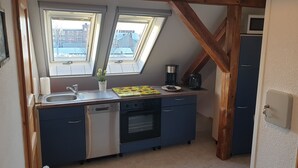 A compact kitchen with a dishwasher, oven, and a coffee maker on the counter. There are two windows providing natural light, and a microwave is visible in the background. - HässelHof - Holiday apartment in the center of Bad Liebenwerda (Bad Liebenwerda)