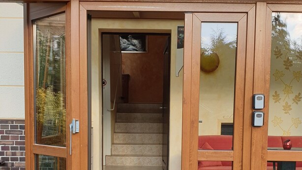 A wooden front door with glass panels, a set of stairs leading inside, and a red bench outside. - HässelHof - Holiday apartment in the center of Bad Liebenwerda (Bad Liebenwerda)