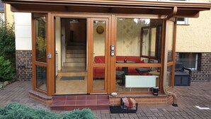 A glass-enclosed entryway with a wooden frame, a red sofa, and a dining table inside. - HässelHof - Holiday apartment in the center of Bad Liebenwerda (Bad Liebenwerda)