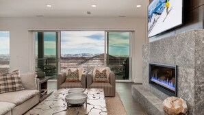 A modern living room with a fireplace, large windows, and a scenic mountain view.