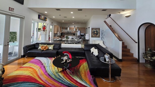 A spacious living area with a black sofa, a colorful rug, a chandelier, and a staircase. - Lands Fine Art Gallery  (Hollywood)