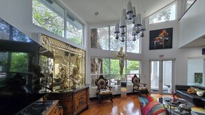 A spacious room with large windows, a chandelier, and a variety of furniture including a sofa, armchair, and a wooden cabinet. - Lands Fine Art Gallery  (Hollywood)